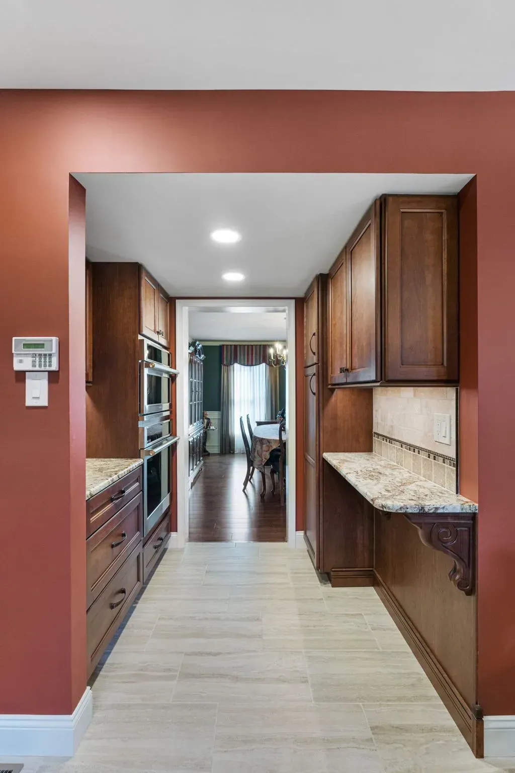 Narrow kitchen hallway with wood cabinets, red walls, and a granite breakfast bar  In Bucks County PA