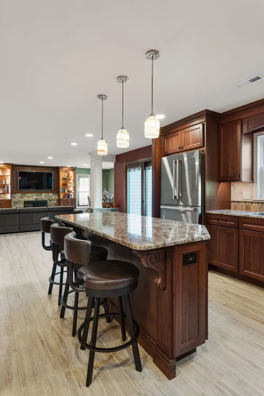 Modern kitchen with granite island, three bar stools, stainless refrigerator, and pendant lights  In Bucks County PA