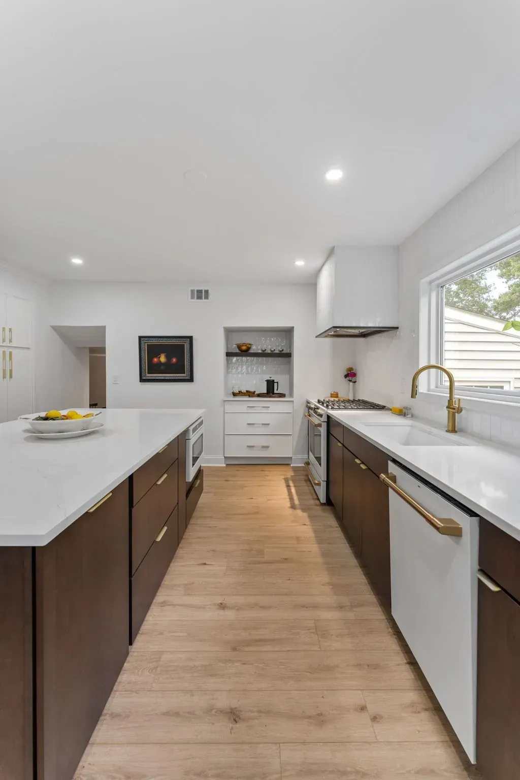 Modern kitchen with white countertops, dark wood cabinets, gold fixtures, and a window over the sink In Bucks County PA