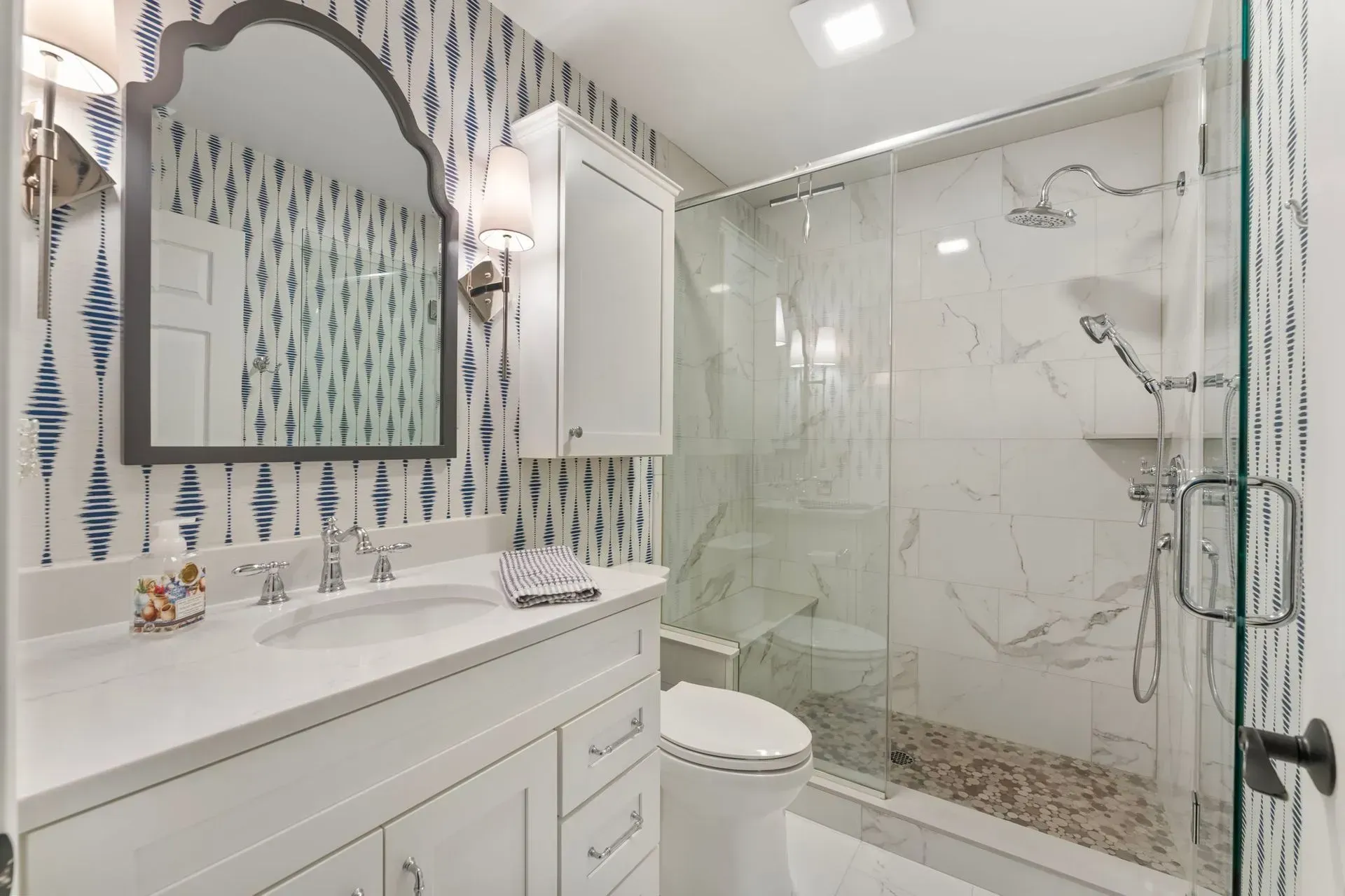 Bright white bathroom with double vanity, decorative mirror, and glass-enclosed shower In Bucks County PA