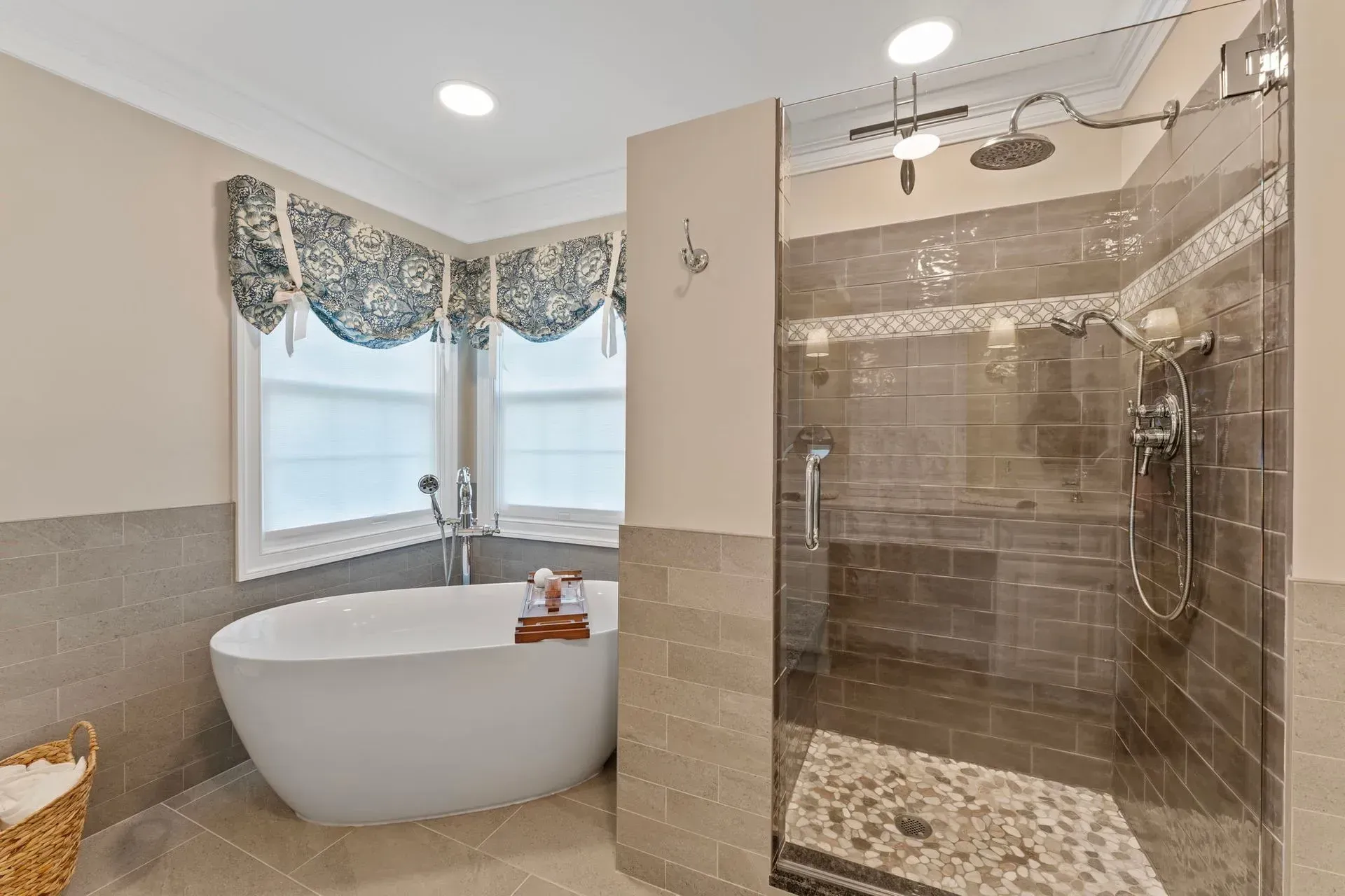 Bright bathroom with freestanding tub, glass shower, beige tile, and window with patterned valance In Bucks County PA