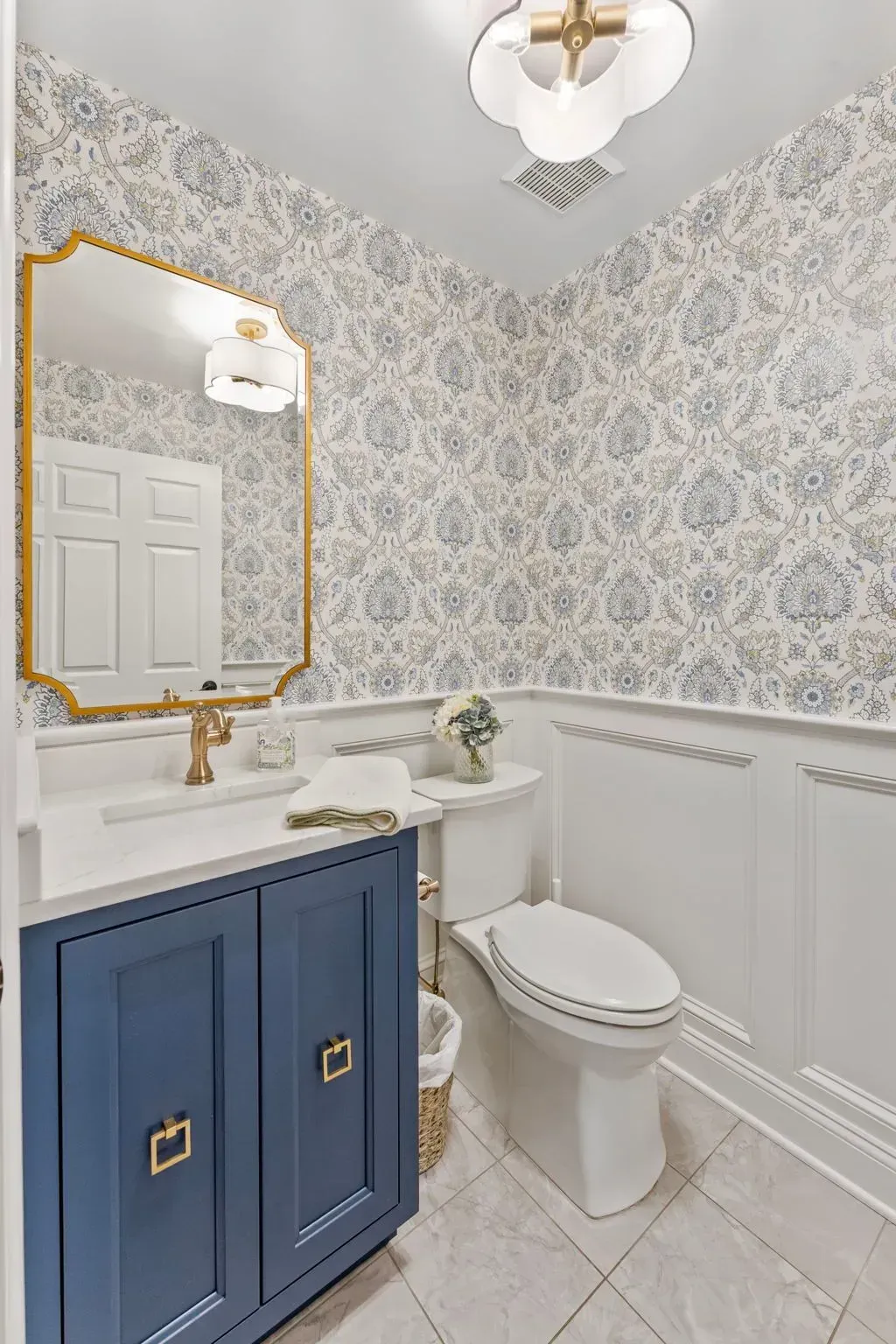 Small elegant bathroom with blue vanity, gold mirror, white toilet, and patterned wallpaper In Bucks County PA