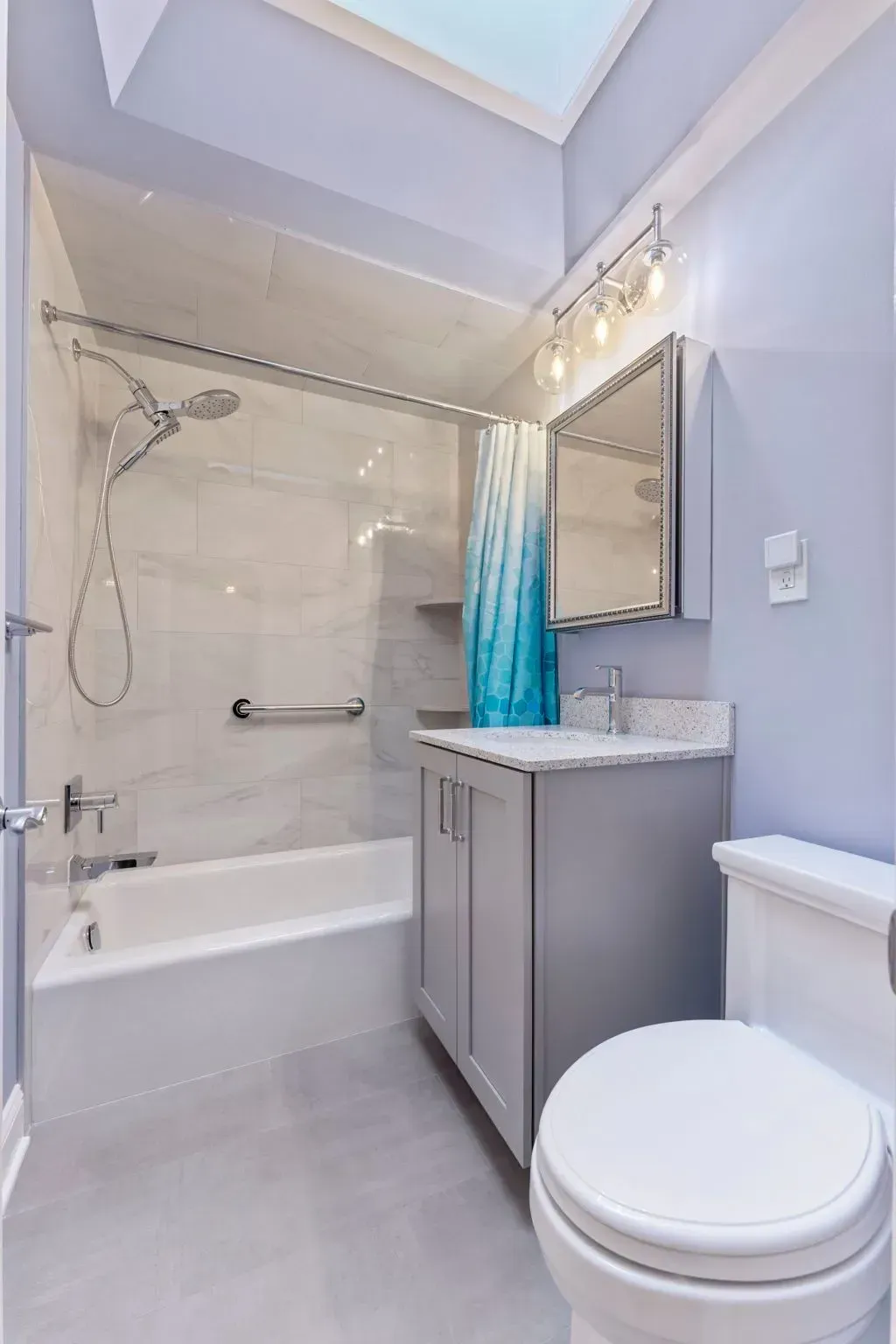 Small modern bathroom with bathtub, vanity, mirror, and toilet in light gray tones  In Bucks County PA