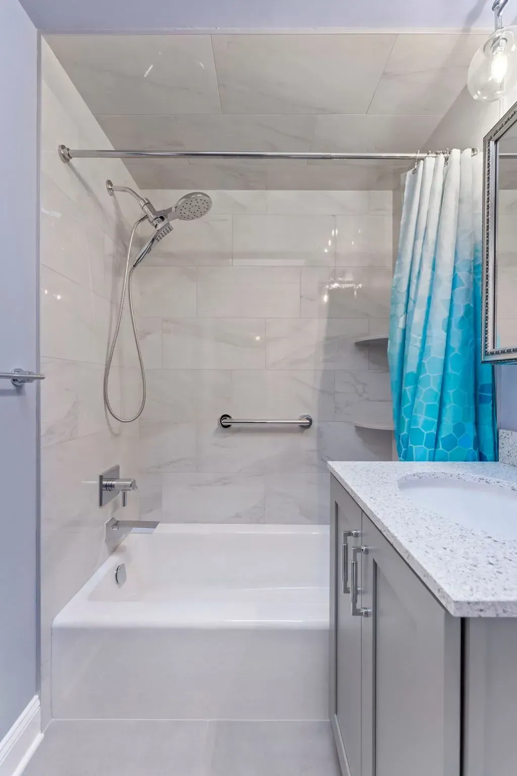 Modern bathroom with white tub, shower curtain, chrome fixtures, and gray vanity with countertop  In Bucks County PA