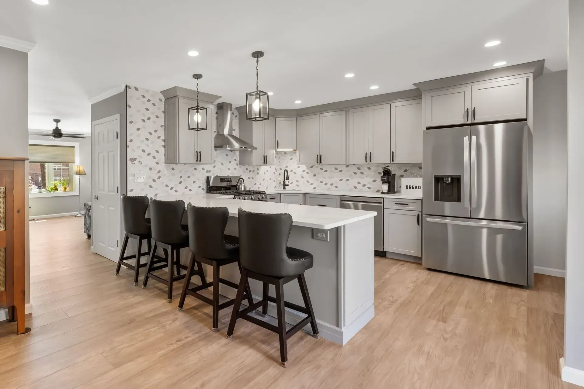 Modern white kitchen with island, black stools, stainless steel appliances, and light wood floors In Bucks Country PA