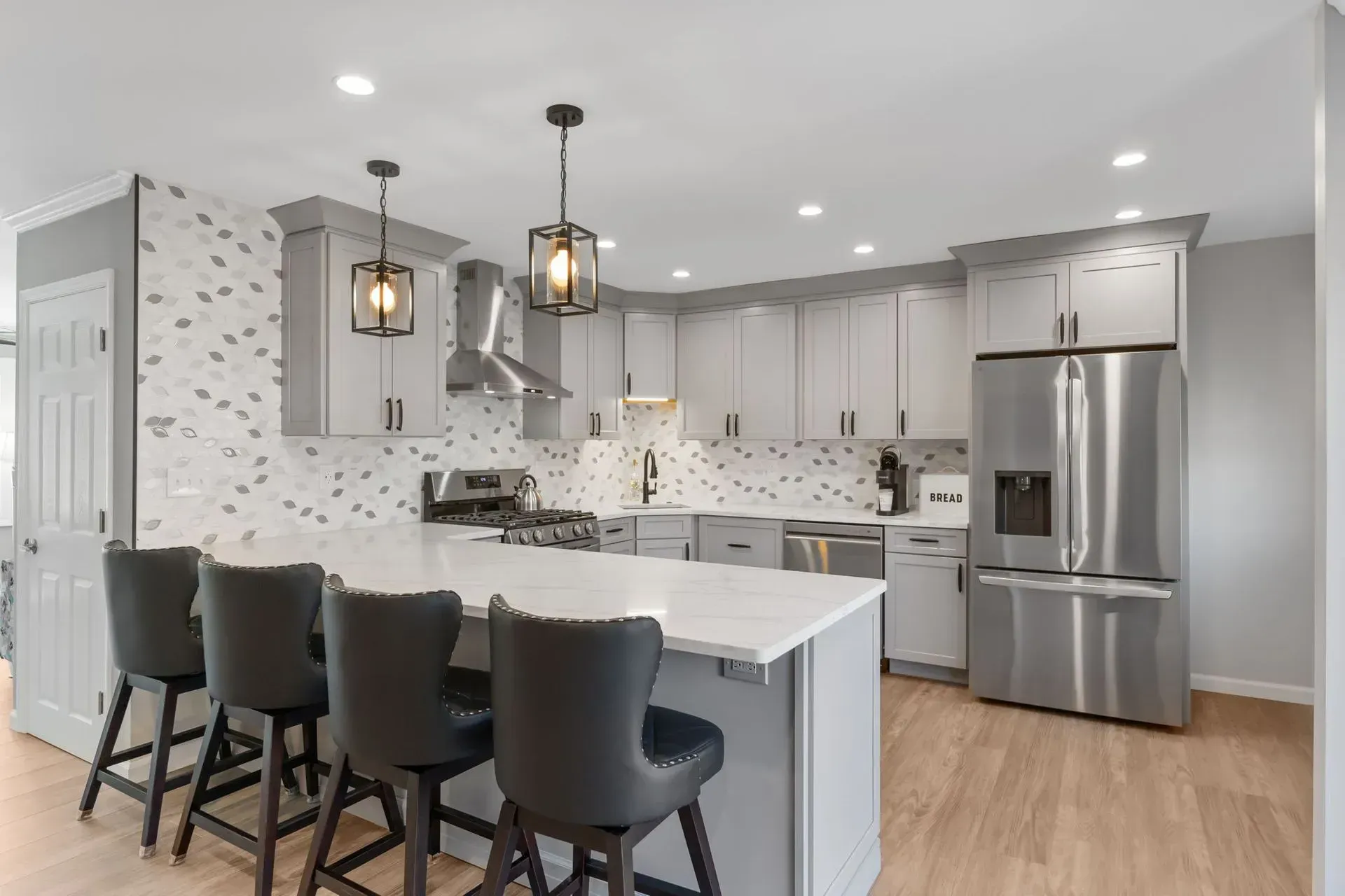 Bright modern kitchen with white cabinets, stainless appliances, island, and four black bar stools In Bucks County PA