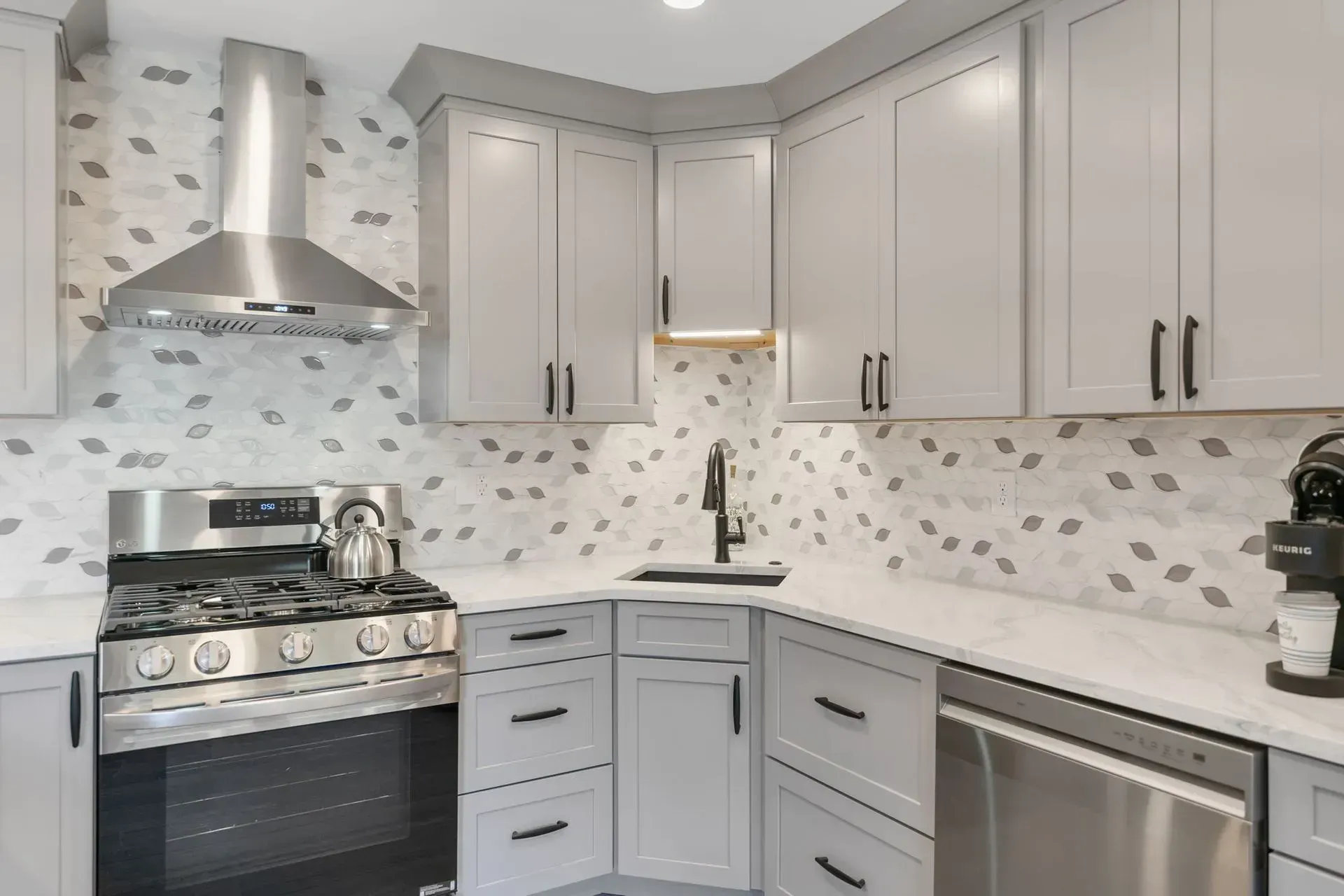 Modern white kitchen with stainless steel stove, sink, dishwasher, and gray tile backsplash In Bucks County PA