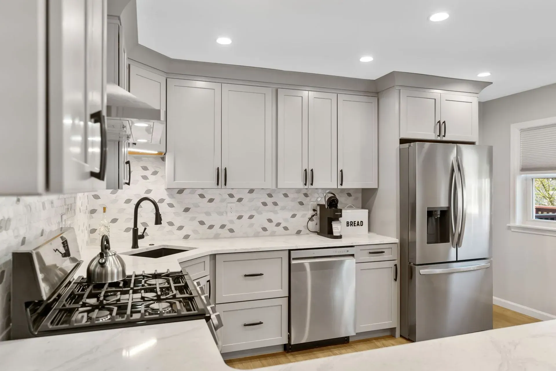 Modern white kitchen with stainless steel appliances, gray cabinets, and marble backsplash In Bucks County PA