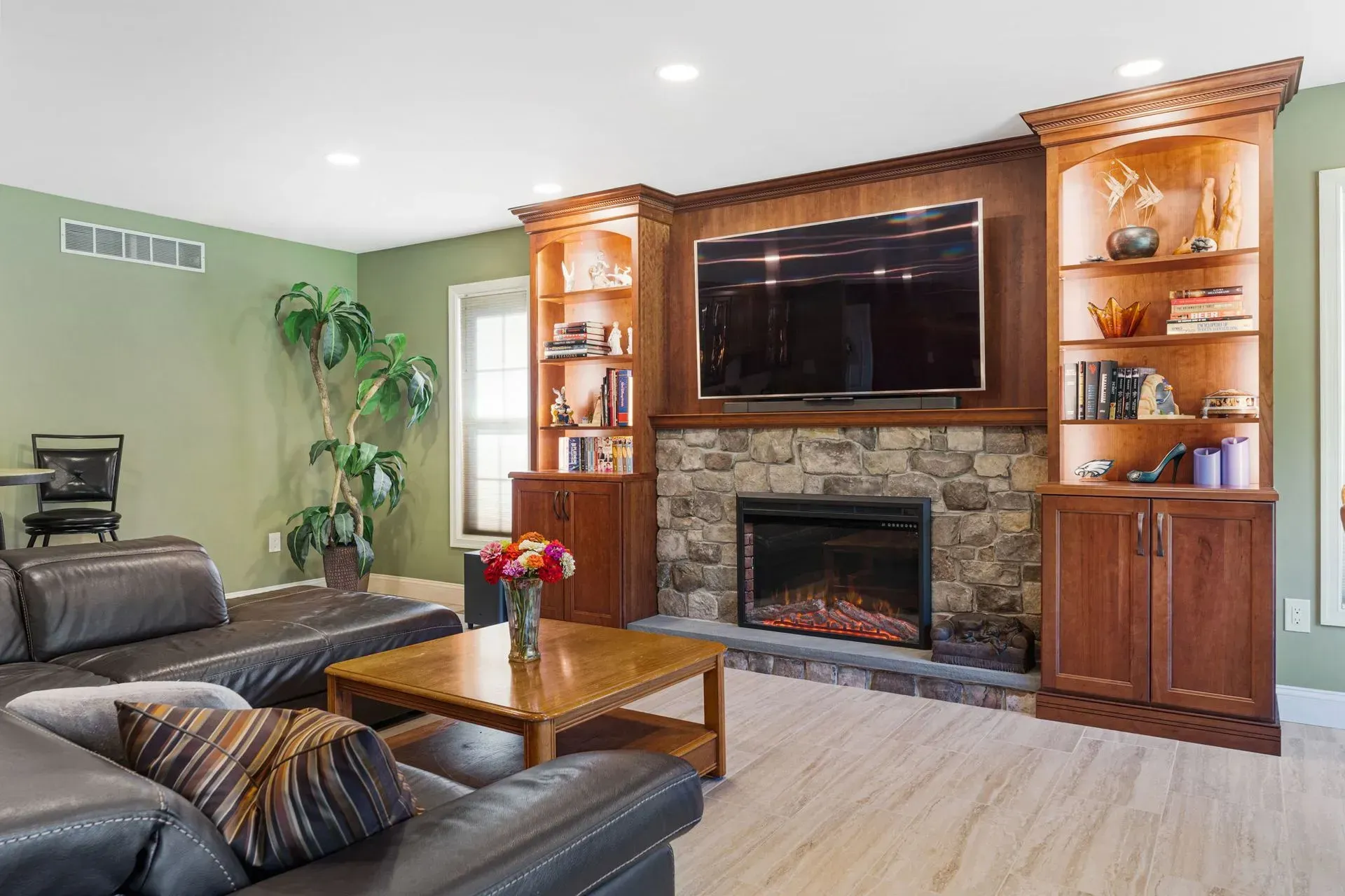 Modern living room with stone fireplace, wall-mounted TV, wood cabinets, and black leather sofa  In Bucks County PA
