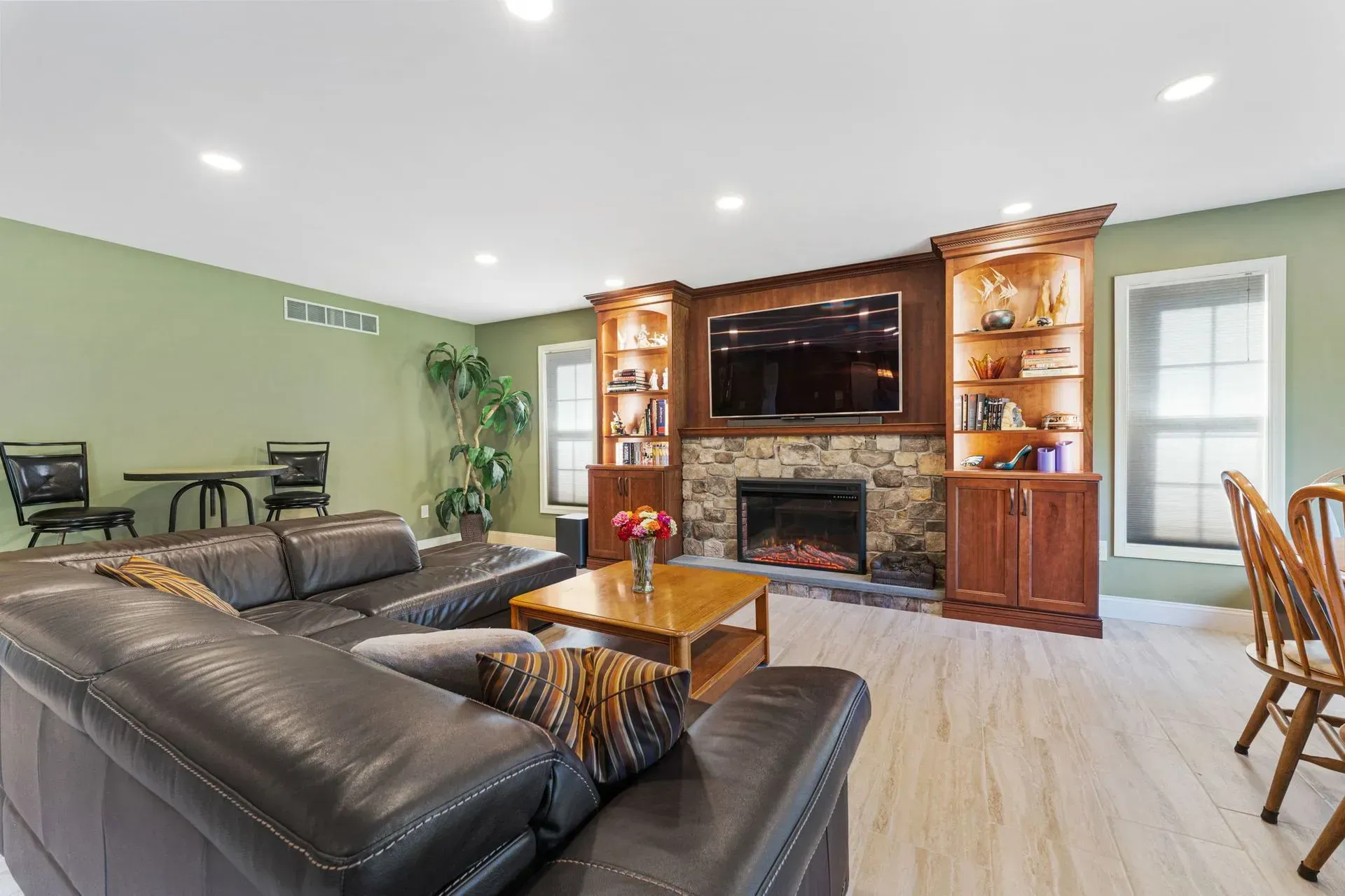 Spacious living room with black leather sofa, fireplace TV wall, hardwood floor, and green walls  In Bucks County PA