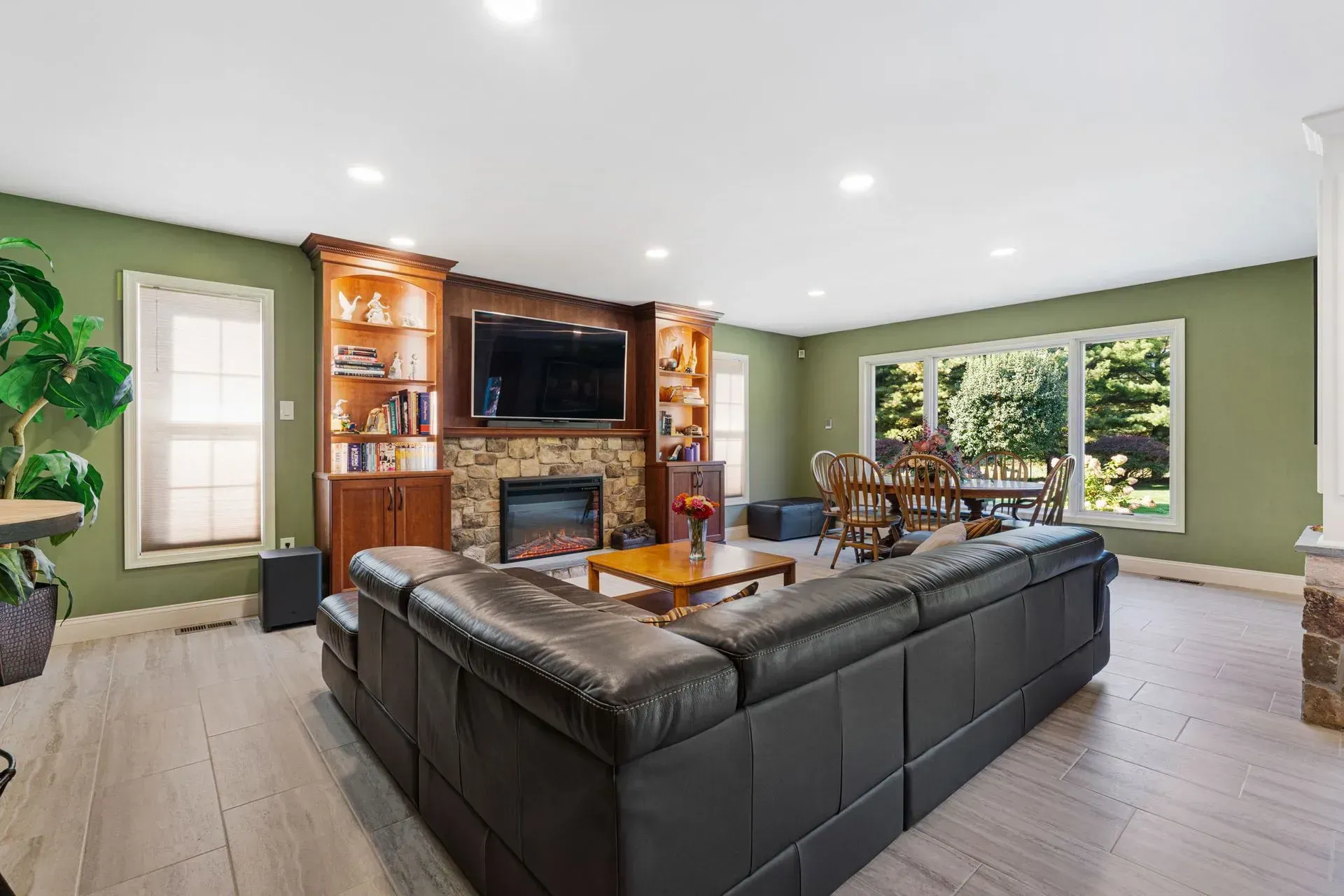 Spacious living room with black sectional sofa, fireplace, TV, green walls, and large windows  In Bucks County PA