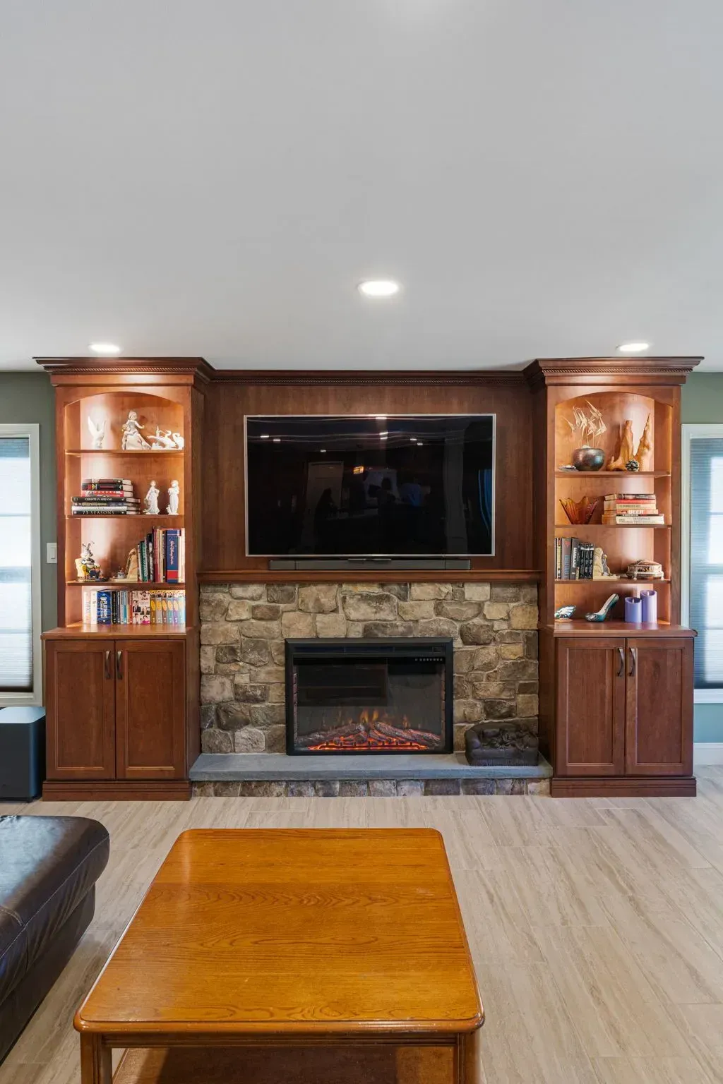 Living room with stone fireplace, wall-mounted TV, wood built-ins, and a coffee table  In Bucks County PA