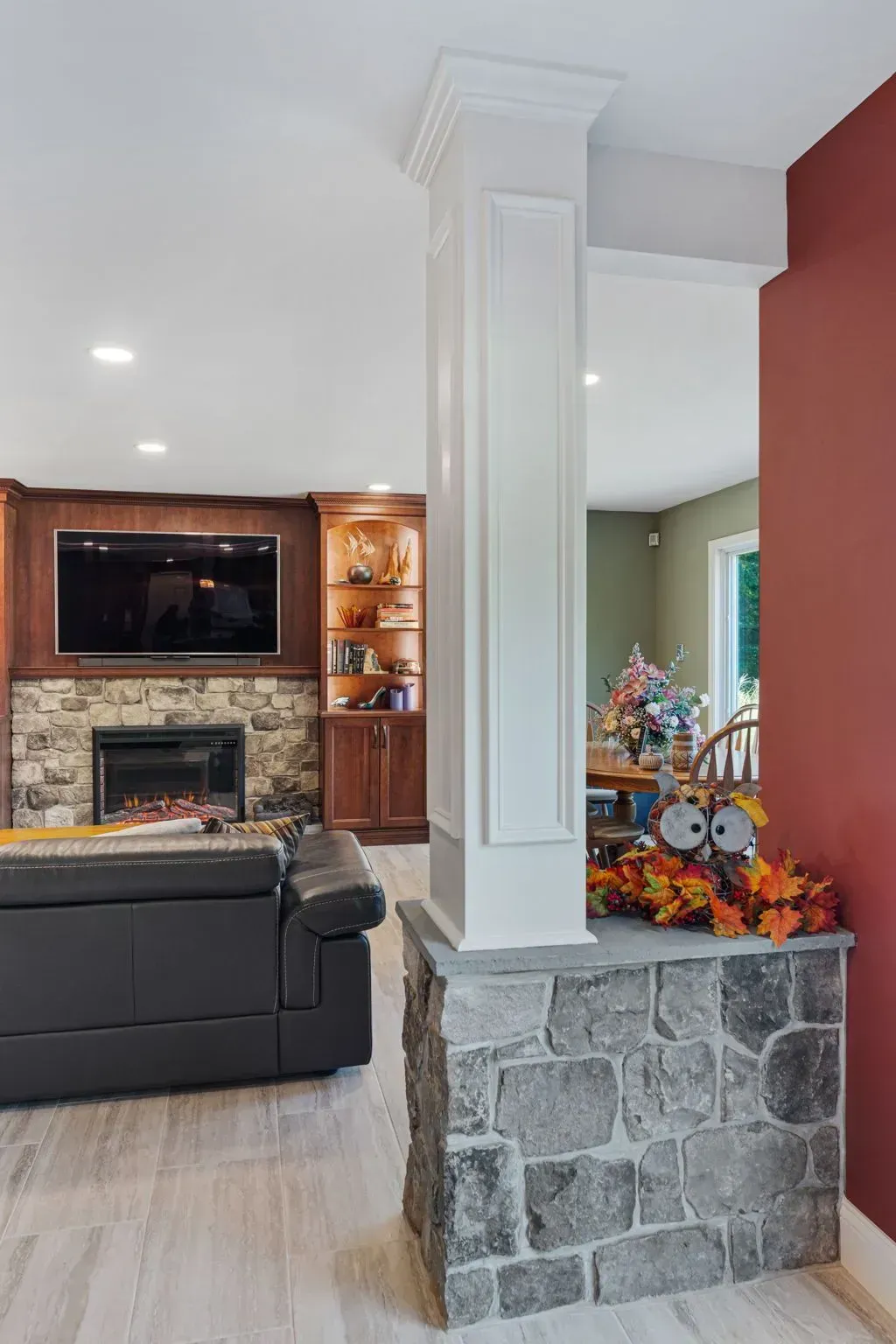 Living room with stone fireplace, dark sofa, white column, and fall decor on a stone half wall  In Bucks County PA