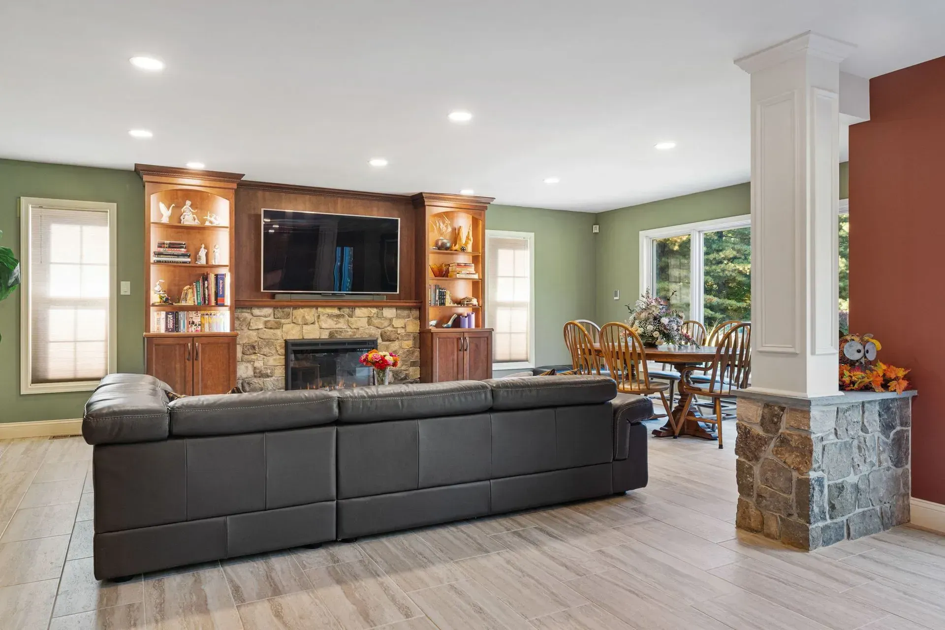 Spacious living room with a black sectional, stone fireplace, wall-mounted TV, and dining area beyond  In Bucks County PA