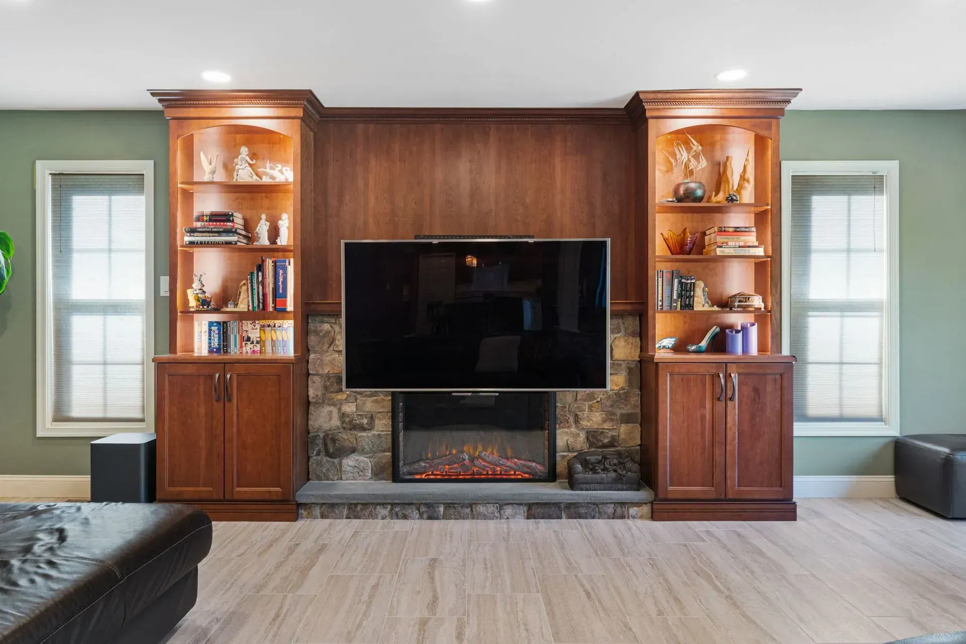 Living room with built-in wood shelves, TV, and stone fireplace between two windows  In Bucks County PA