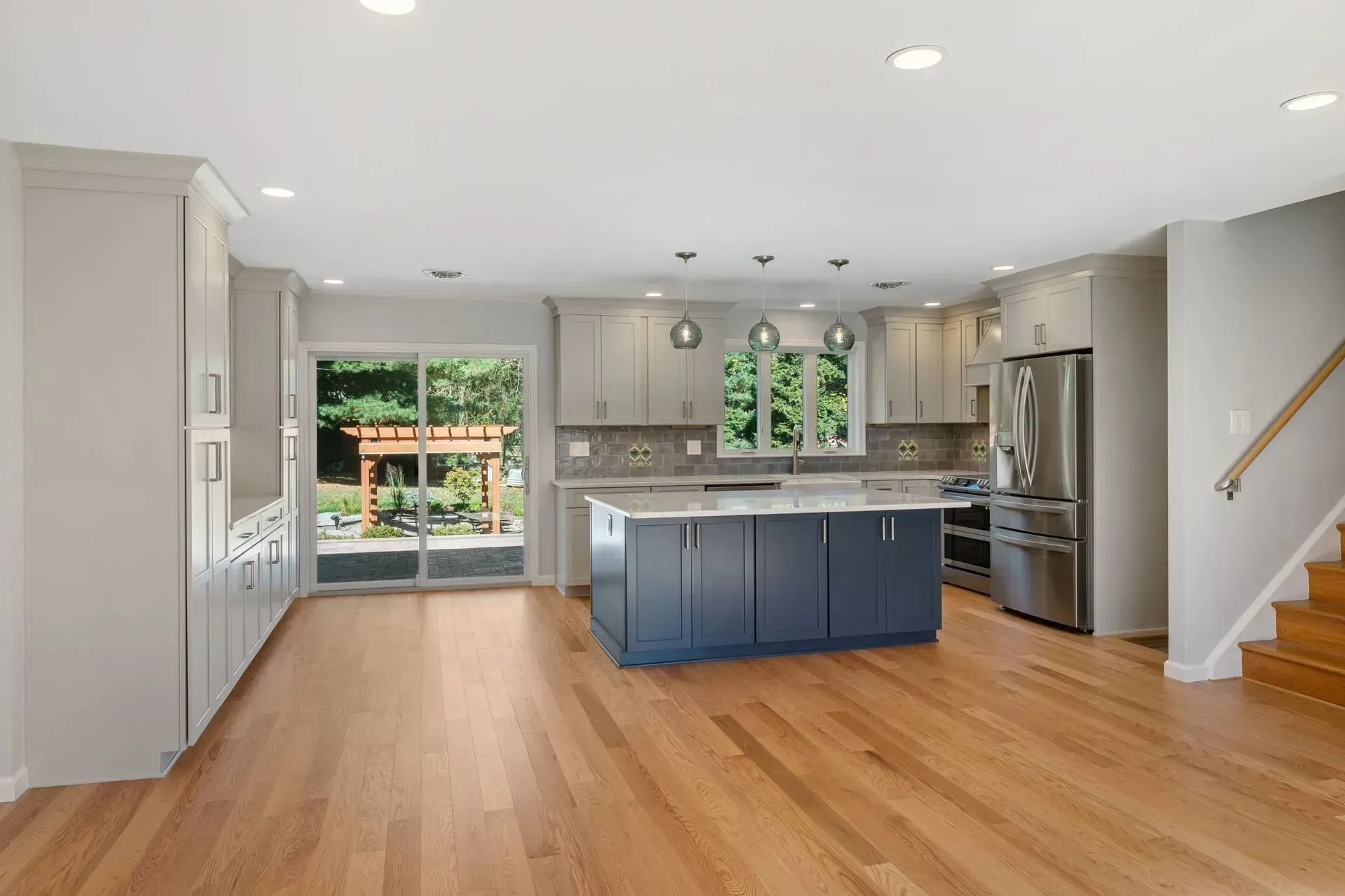 Bright modern kitchen with blue island, wood floors, stainless appliances, and staircase nearby  In Bucks County PA