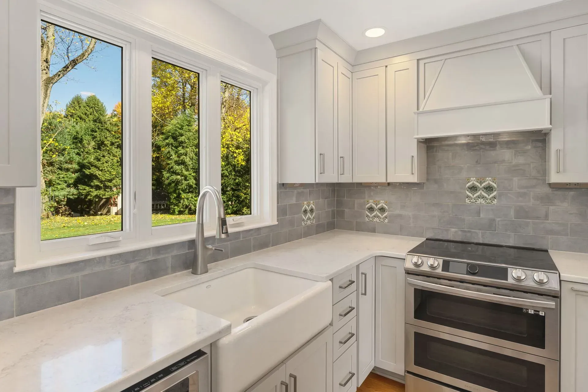 Bright modern kitchen with white cabinets, gray tile backsplash, stainless stove, and large window over the sink  In Bucks County PA