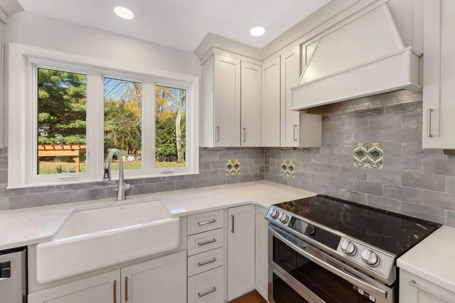 Bright modern kitchen with white cabinets, farmhouse sink, granite countertops, and stainless steel stove by a window  In Bucks County PA