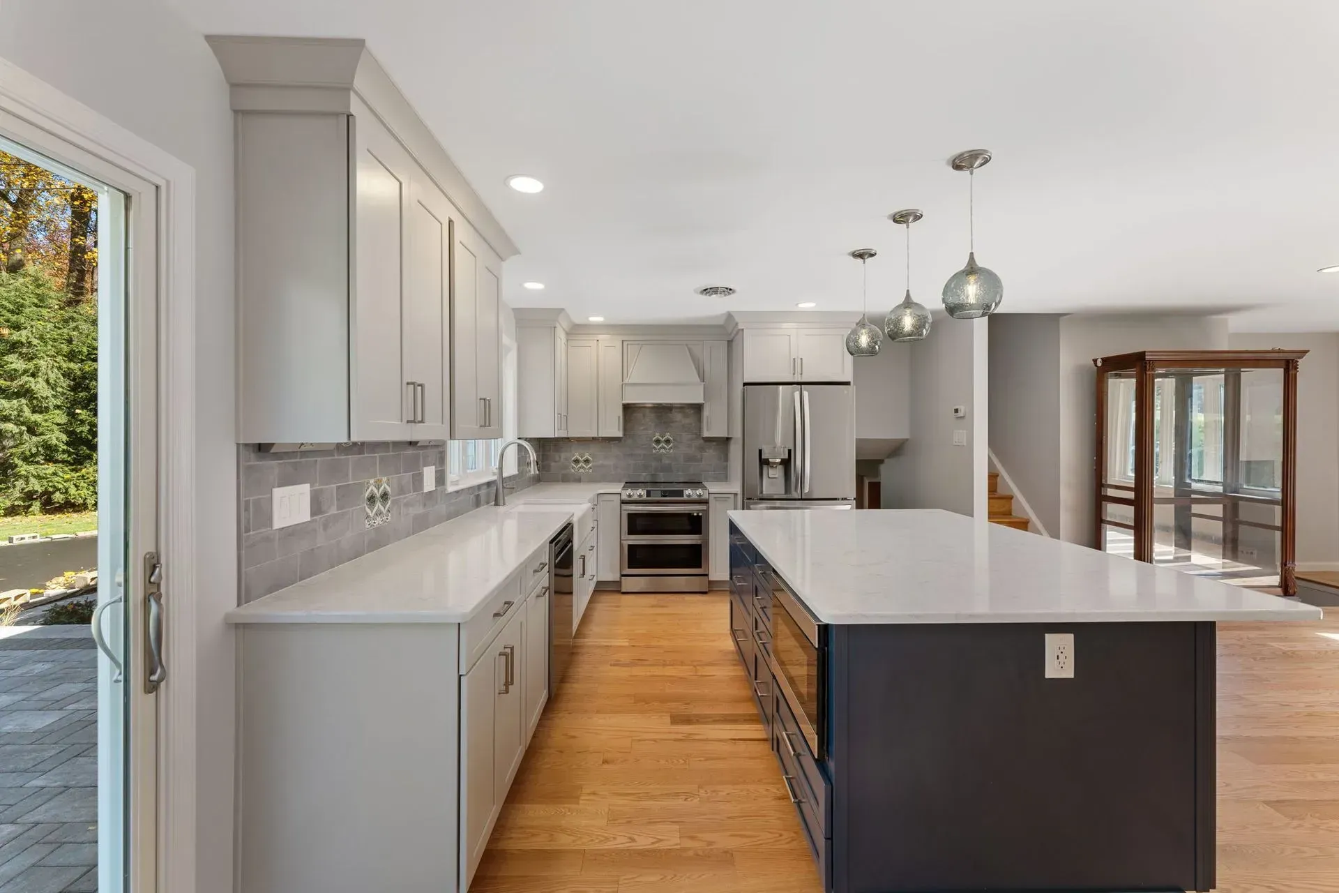 Bright modern kitchen with gray cabinets, white countertops, and a dark island opening to a dining area  In Bucks County PA