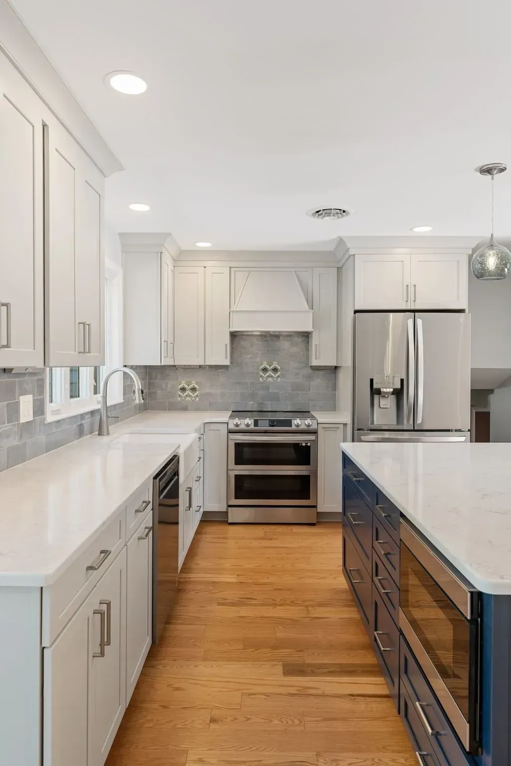 Bright modern white kitchen with stainless steel appliances and wood floor, viewed from the island  In Bucks County PA