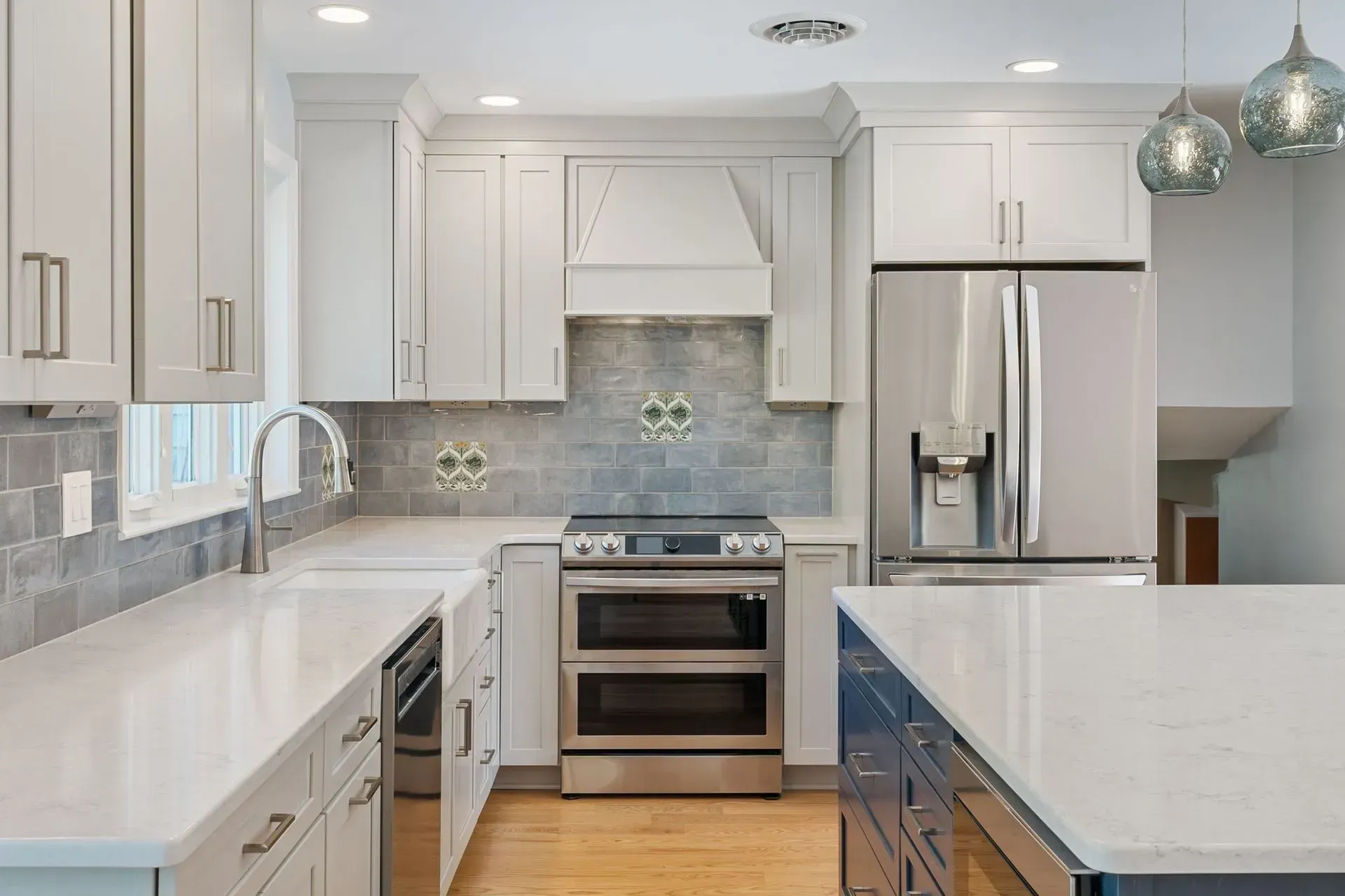 Modern white kitchen with stainless steel appliances, marble island, and pendant lights  In Bucks County PA