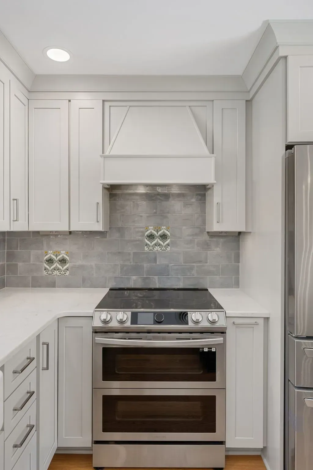 Modern white kitchen with stainless steel range and hood, gray tile backsplash, and light countertops  In Bucks County PA