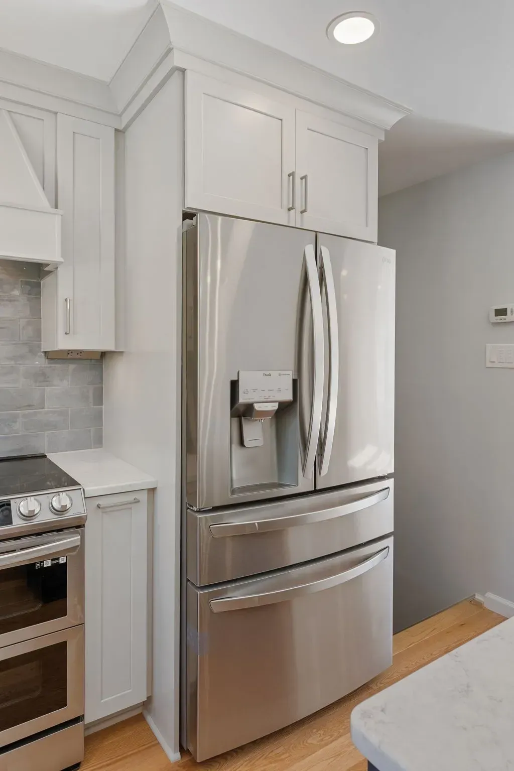 Modern kitchen with stainless steel French-door refrigerator, white cabinets, and a stove on the left  In Bucks County PA