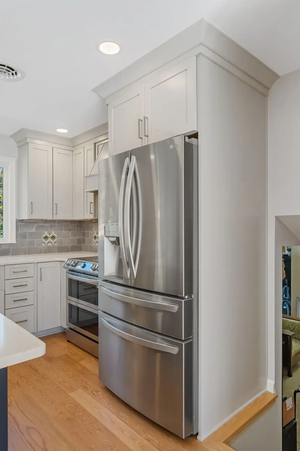 Modern white kitchen with stainless steel refrigerator, oven, and light wood floor  In Bucks County PA