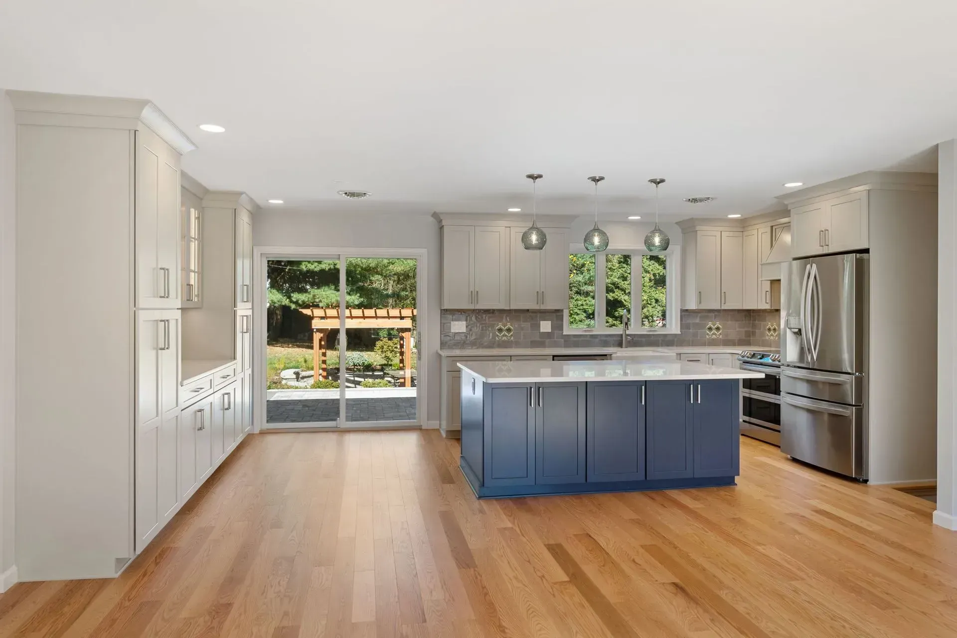 Bright modern kitchen with blue island, stainless steel appliances, hardwood floors, and a sliding door to the backyard  In Bucks County PA