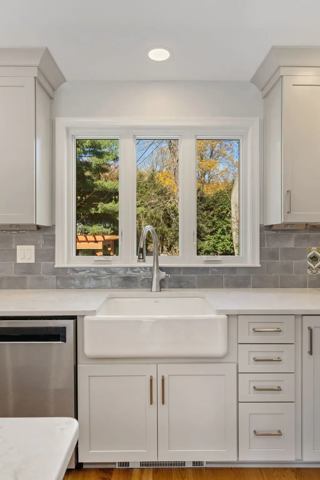 Bright white kitchen sink under window, with gray tile backsplash and stainless dishwasher  In Bucks County PA