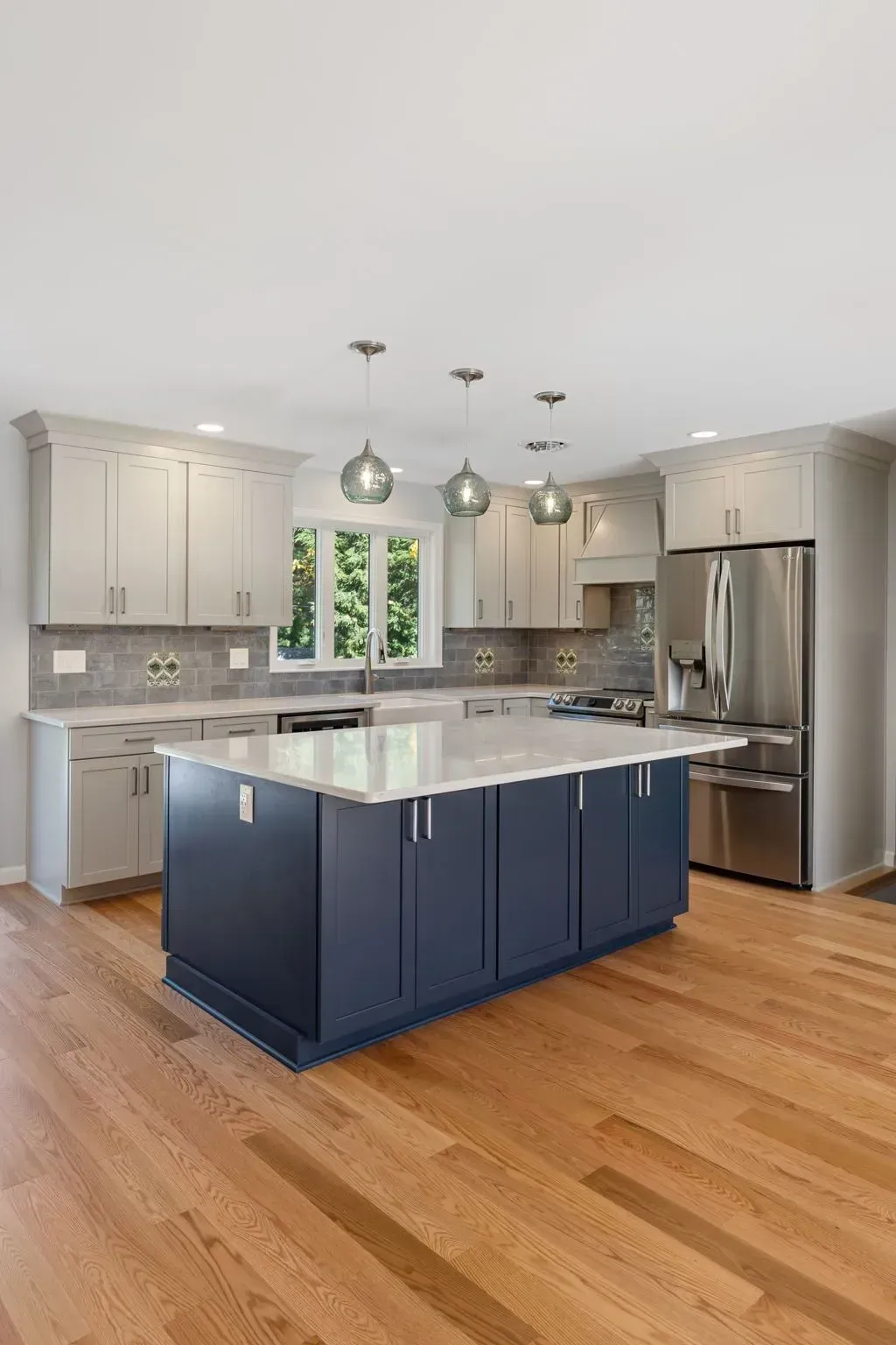 Bright modern kitchen with navy island, white cabinets, stainless steel appliances, and hardwood floors  In Bucks County PA