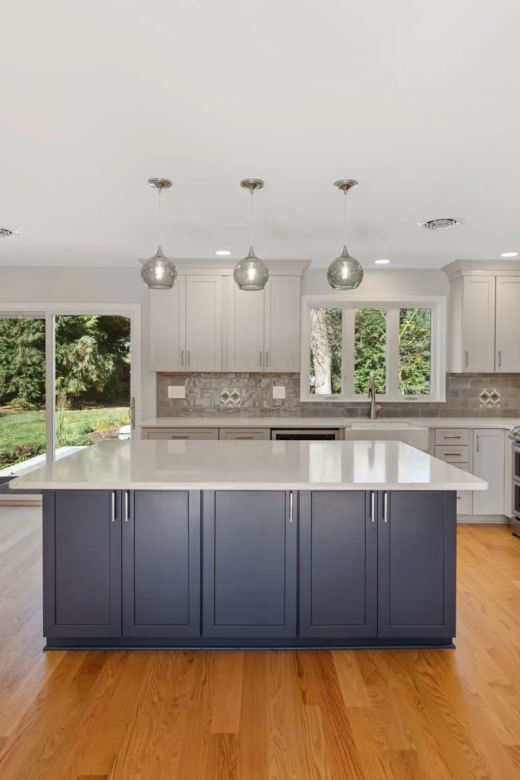 Modern kitchen with blue island, white cabinets, pendant lights, and wood floors  In Bucks County PA