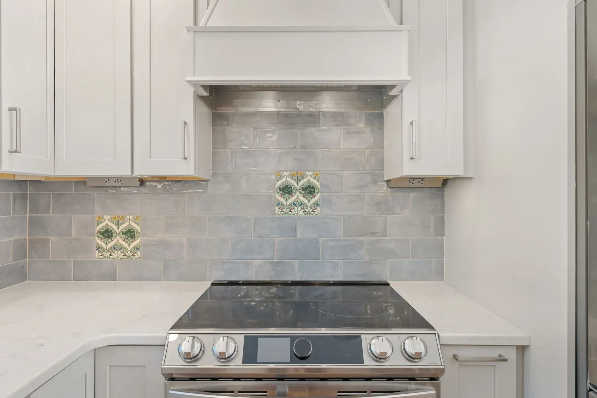Modern kitchen with stainless steel stove, white cabinets, and light gray tile backsplash with decorative accents  In Bucks County PA