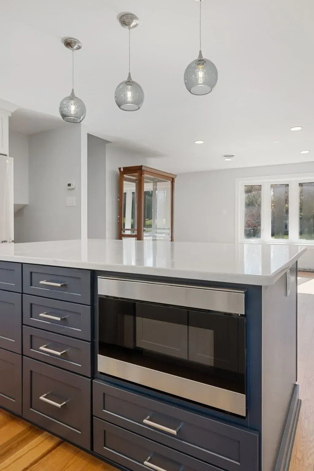 Modern kitchen with dark cabinets, white island, stainless oven, and three pendant lights  In Bucks County PA