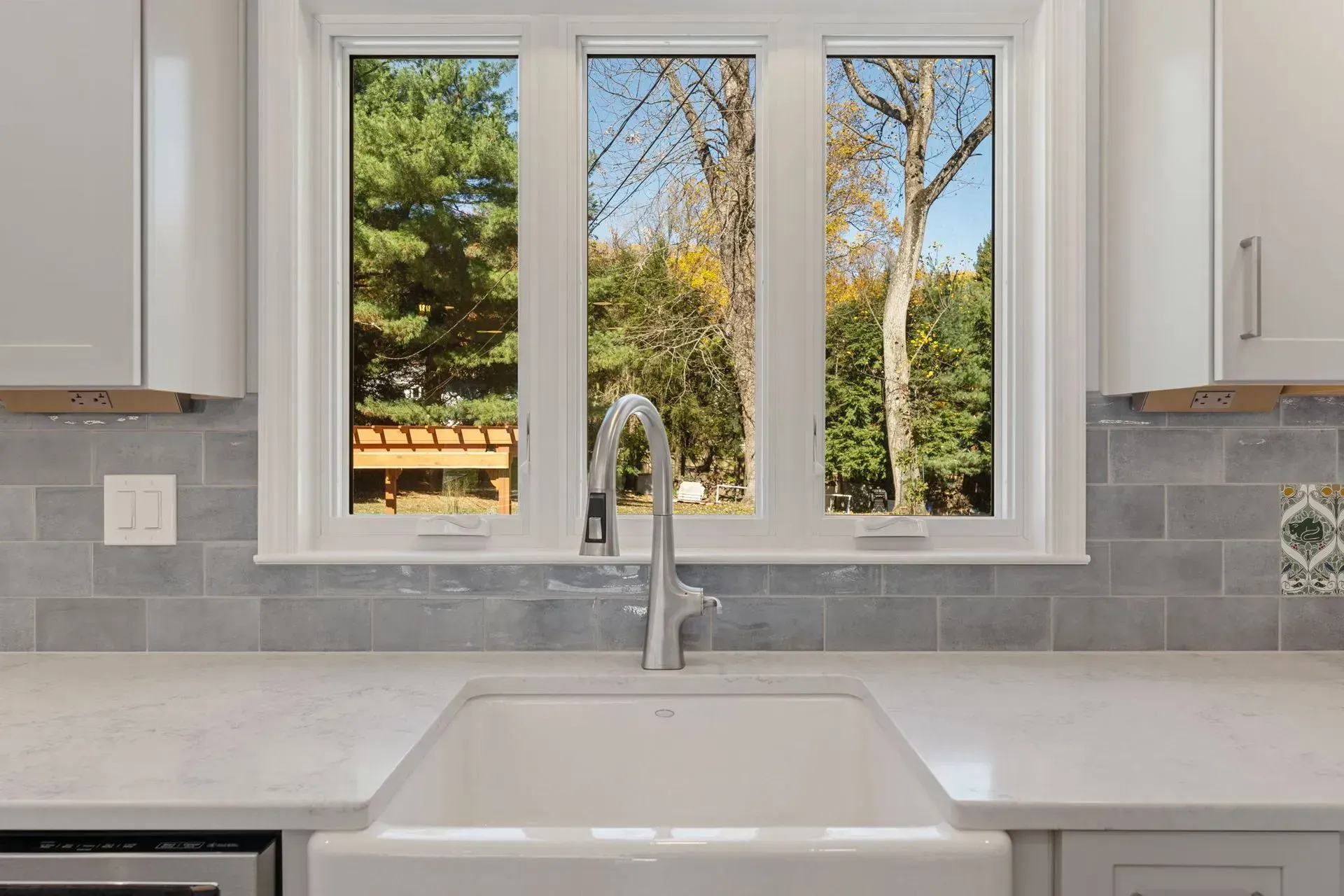 White kitchen sink beneath a window overlooking a sunny backyard garden  In Bucks County PA