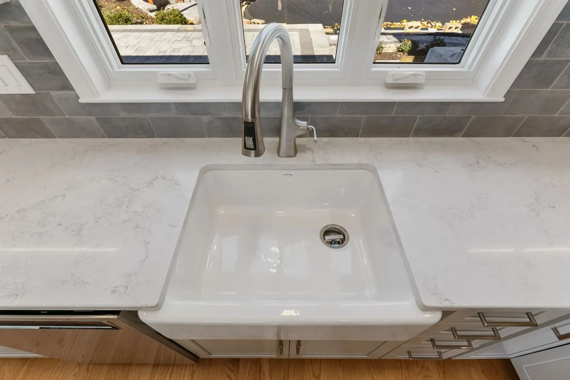 White kitchen sink beneath a window, with a chrome faucet and light gray countertop  In Bucks County PA