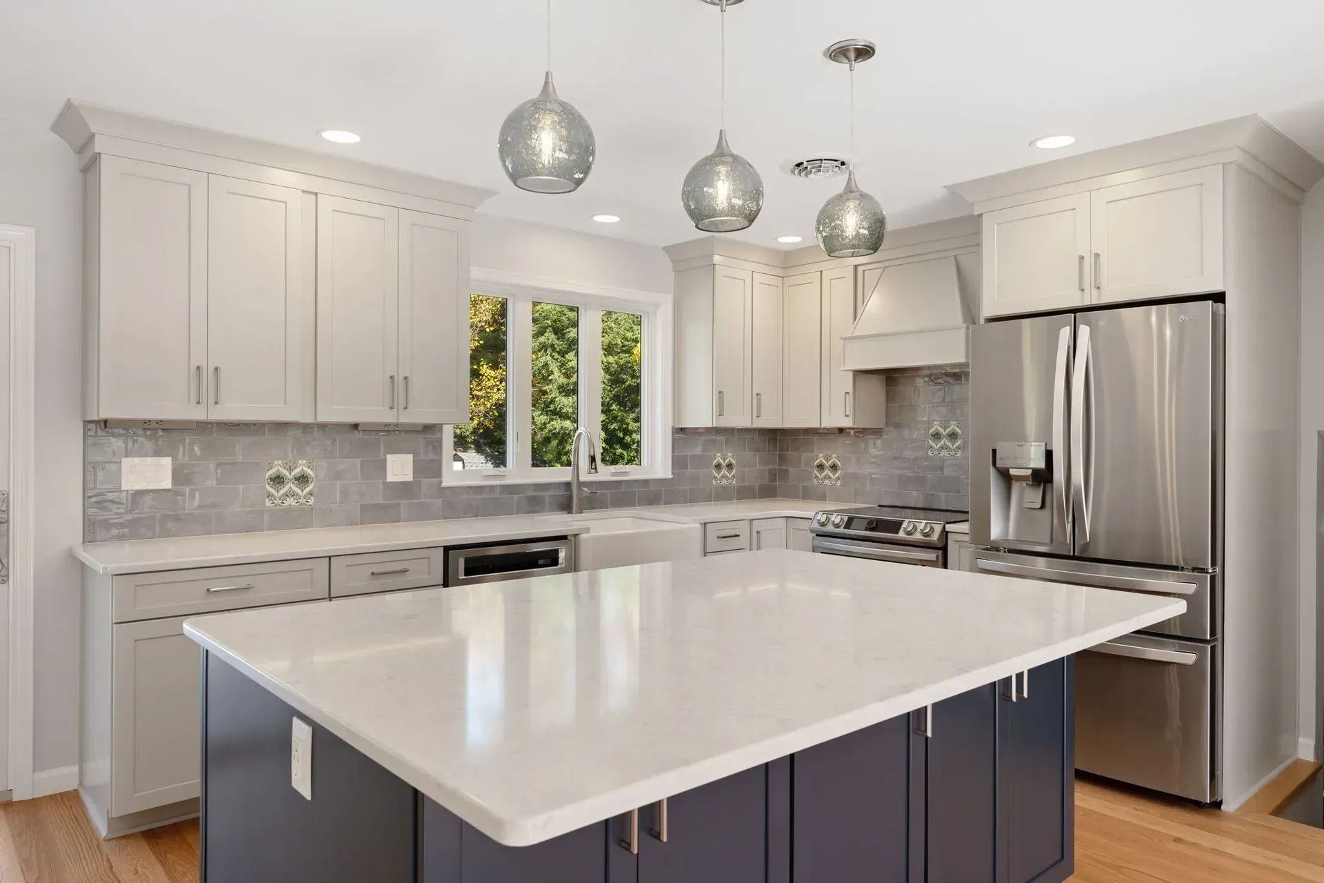 Modern white kitchen with large island, stainless steel appliances, and pendant lights