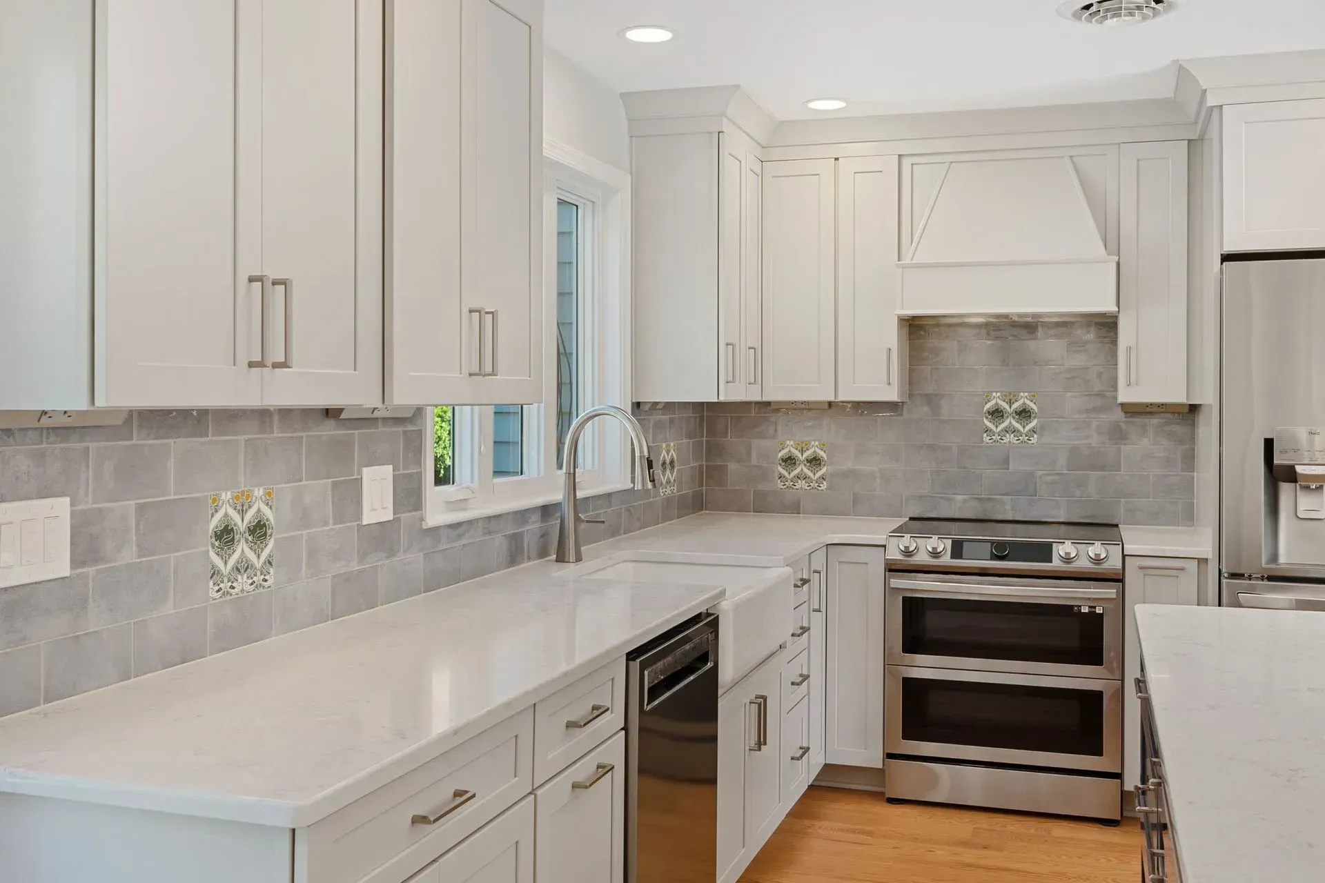 Bright white kitchen with gray tile backsplash, stainless steel stove, and long counter with double sink  In Bucks County PA