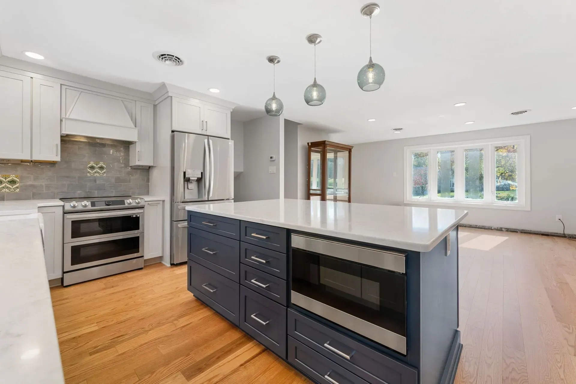 Bright modern kitchen with white cabinets, gray subway tile, wood floors, and a dark island with pendant lights  In Bucks County PA
