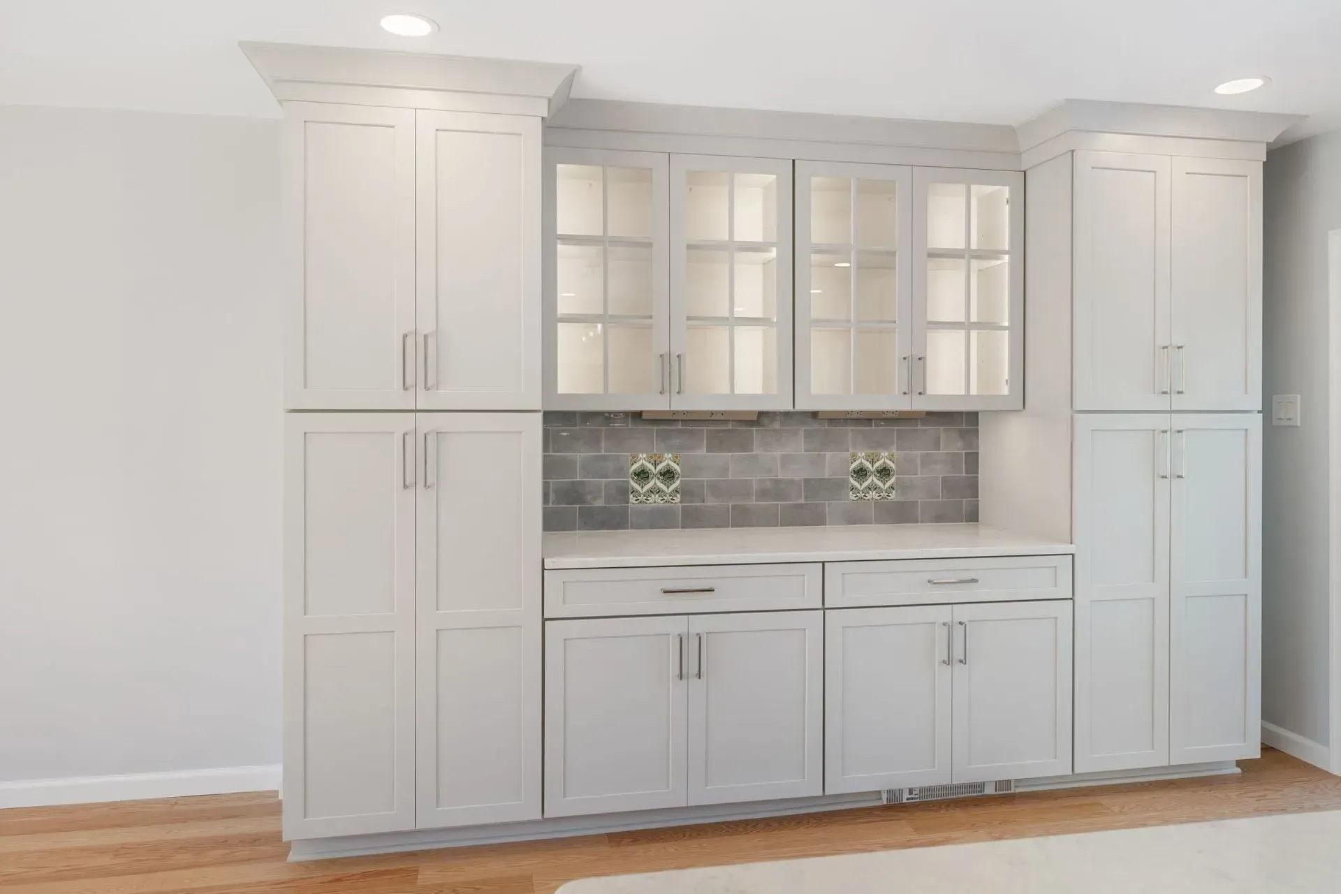Built-in white kitchen cabinets with glass-front uppers and tiled backsplash against a wall  In Bucks County PA