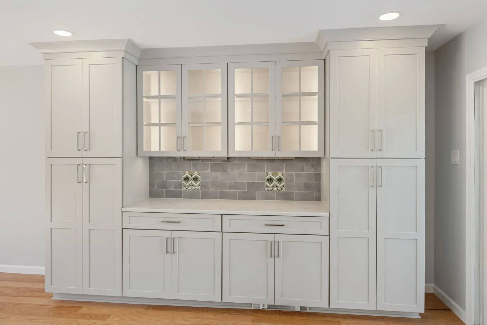 Built-in white kitchen cabinetry with glass-front upper cabinets and gray tile backsplash  In Bucks County PA