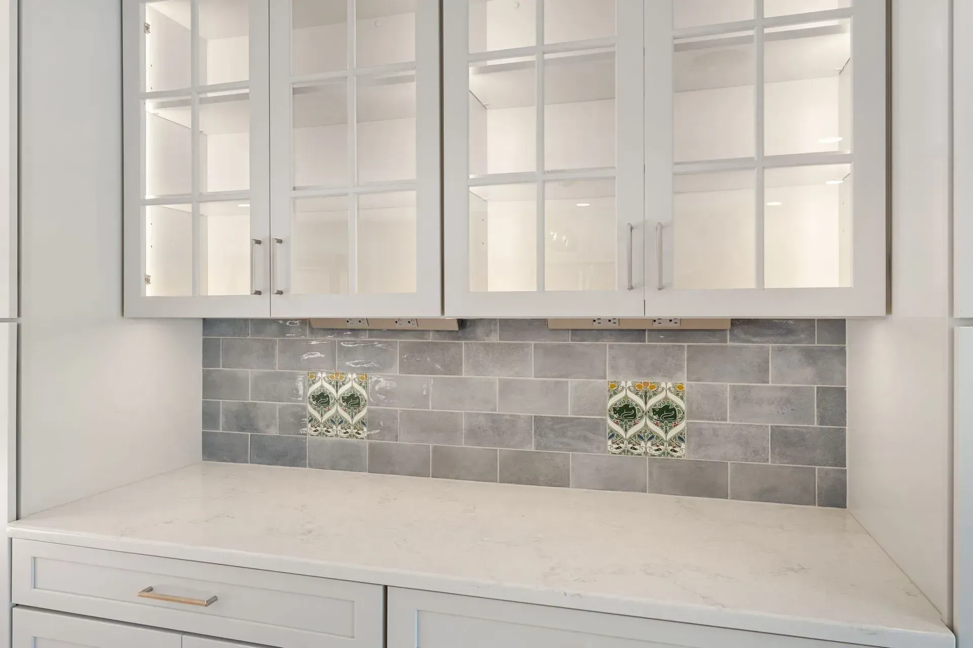 Built-in white cabinets above a white countertop with gray tile backsplash and decorative accent tiles  In Bucks County PA