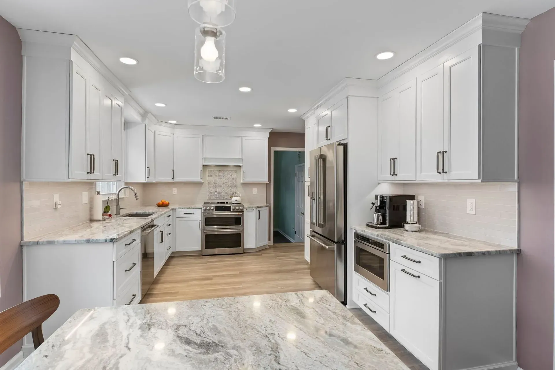 Bright modern white kitchen with marble countertops, stainless appliances, and wood flooring In Bucks Country PA