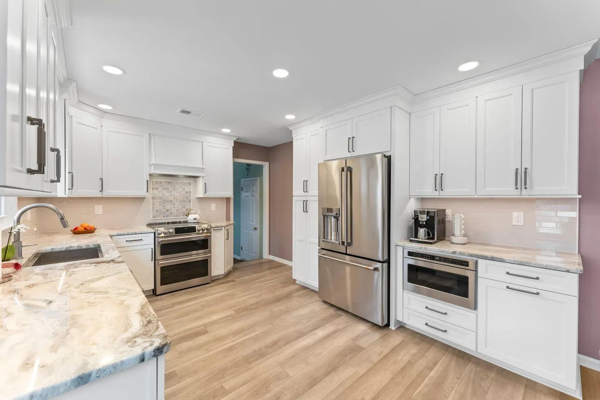Bright white modern kitchen with stainless steel appliances, marble counters, and light wood floors In Bucks County PA