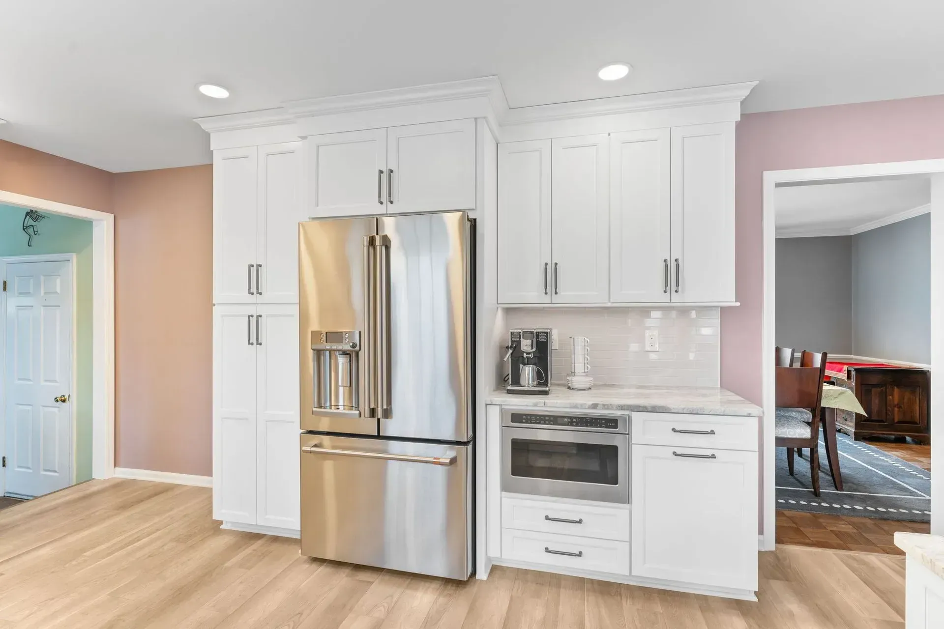 Bright kitchen with white cabinets, stainless steel fridge, built-in oven, and light wood floors In Bucks County PA