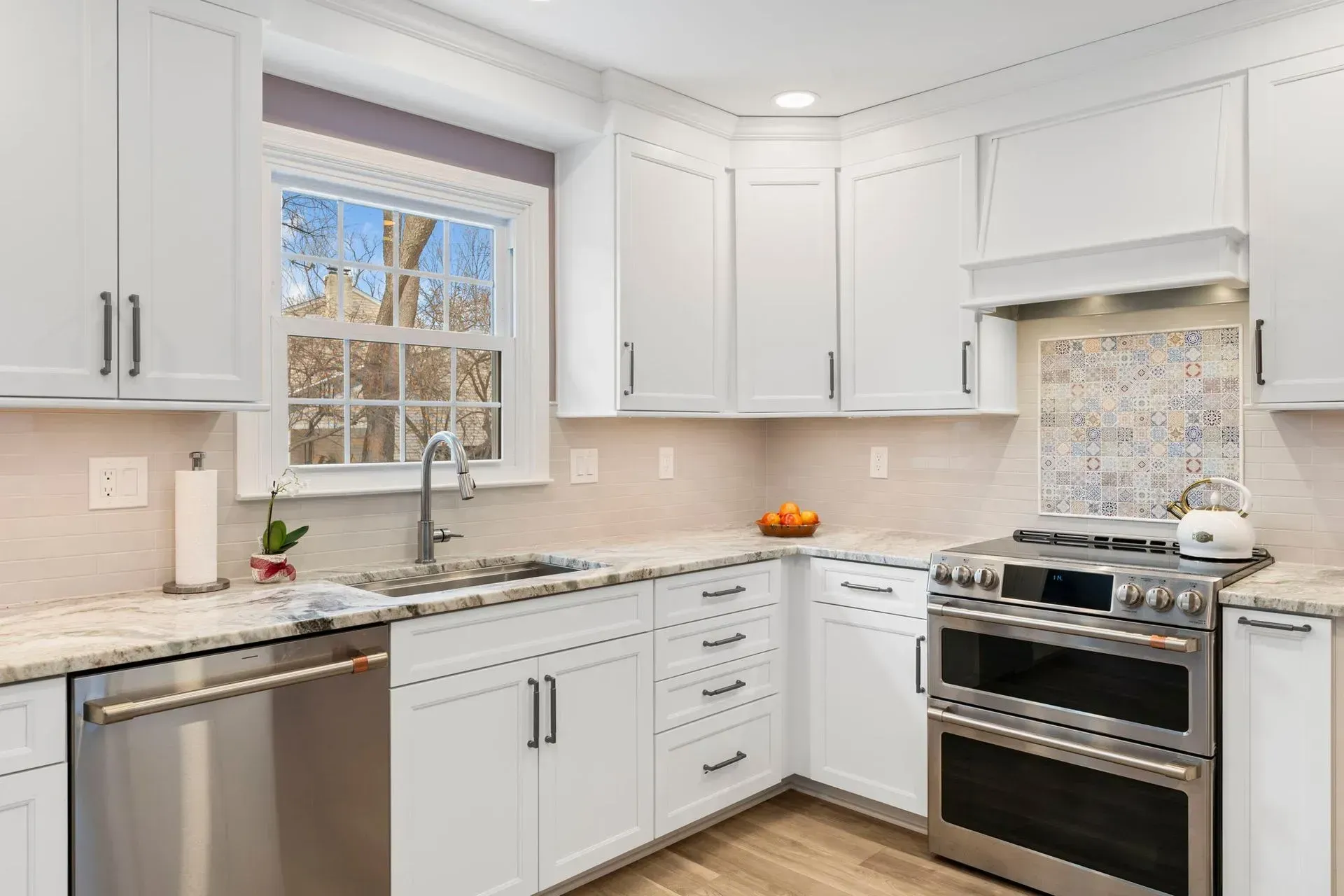 Bright modern white kitchen with stainless steel stove, sink under window, and tiled backsplash In Bucks County PA