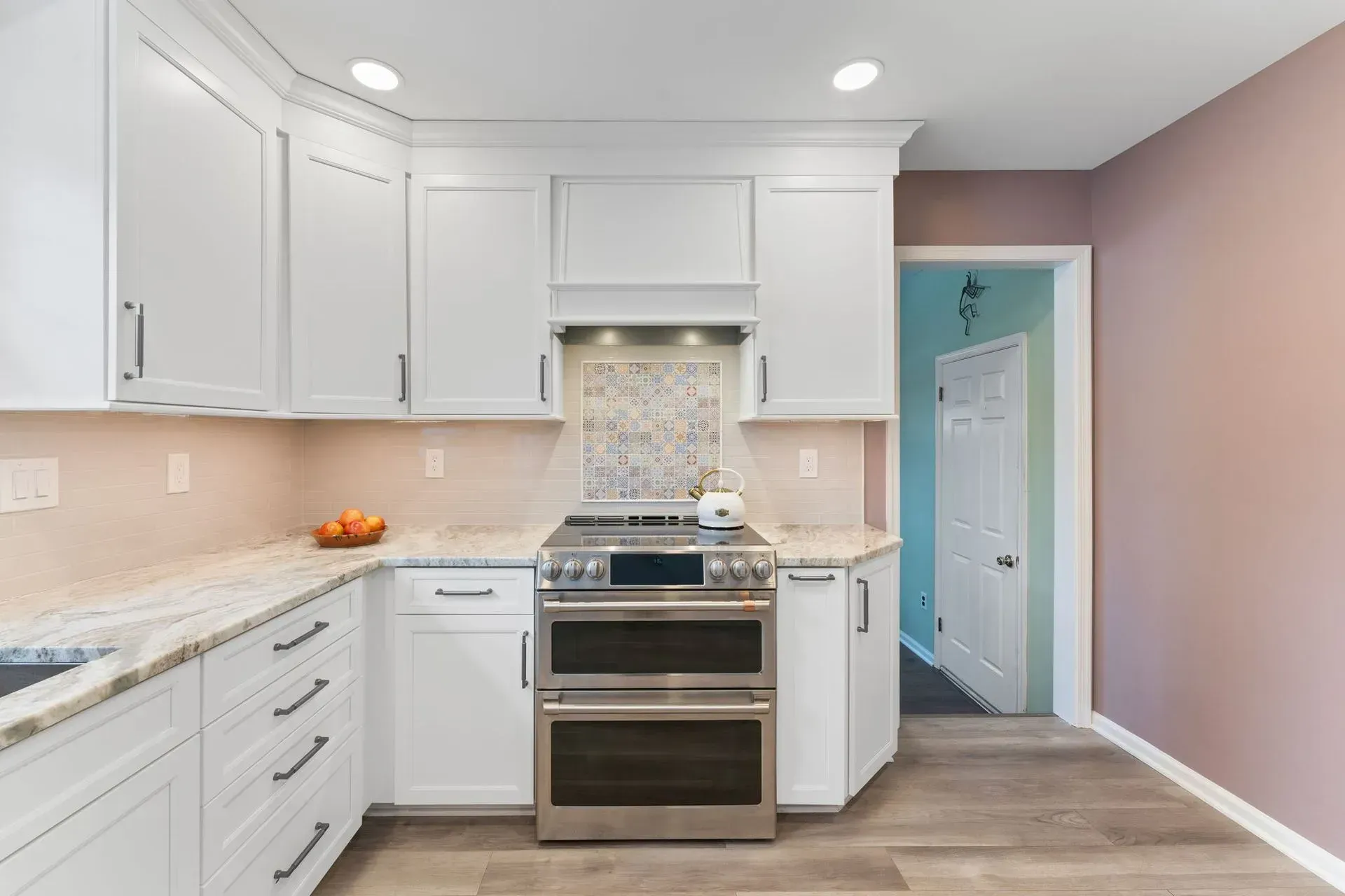 Bright white kitchen with stainless steel stove, light counters, and a pastel pink wall leading to a blue doorway In Bucks County PA