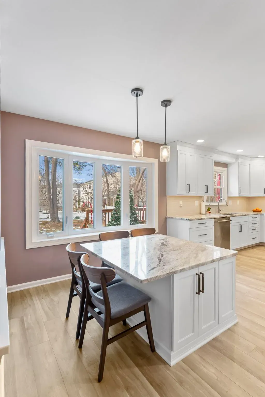 Modern kitchen with white cabinets, marble island, dark chairs, and large windows overlooking trees In Bucks County PA