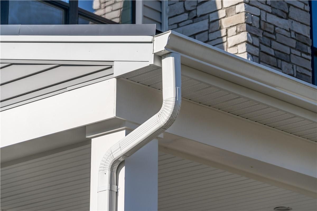 White gutter and downspout on a beige house exterior with brick siding above