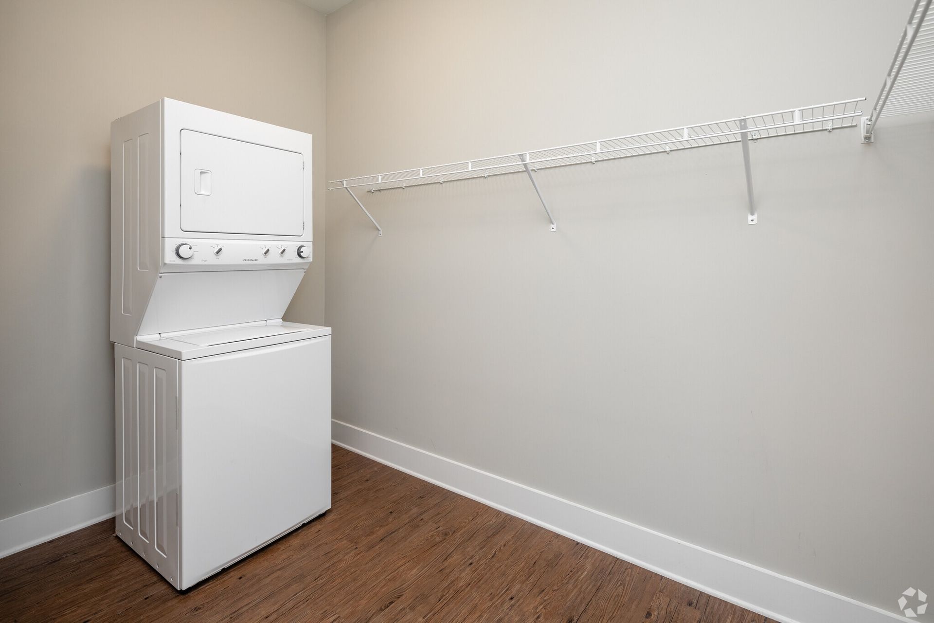 Stacked washing machine and dryer in a small laundry closet with a white wire shelf.